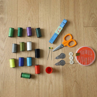 Various colorful thread spools, orange scissors, a blue measuring tape, pins, buttons, and a needle case are arranged on a
