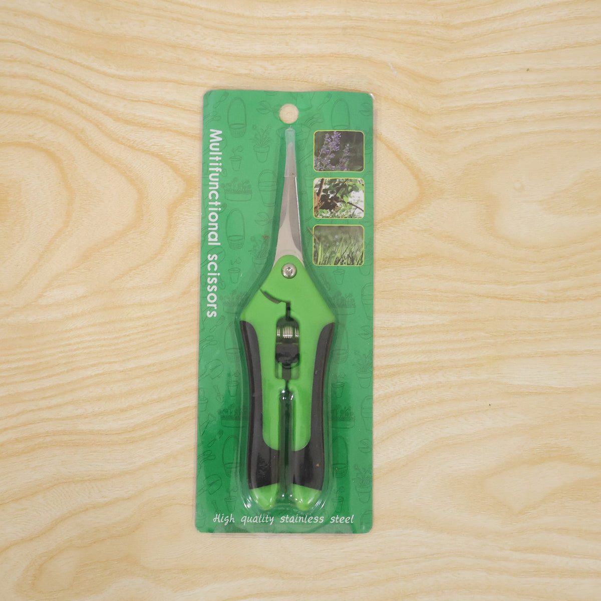 Green and black multifunctional scissors in clear plastic packaging with green backing, displayed on a light wooden surface.