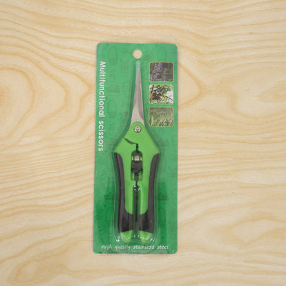 Green and black multifunctional scissors in clear plastic packaging with green backing, displayed on a light wooden surface.