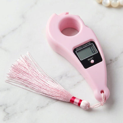 Pink digital finger ring beads counter with a matching pink tassel, shown on a white marble surface.