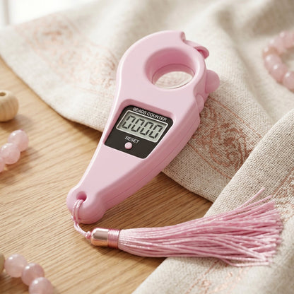 Pink digital beads counter with a tassel resting on a patterned white and gold fabric next to pink beaded bracelets.
