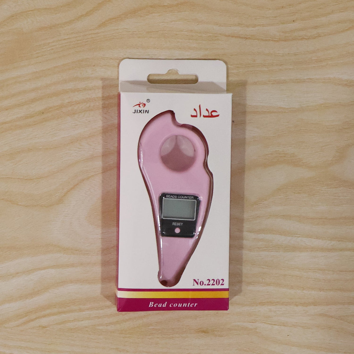 The pink digital beads counter packaged in a white and pink box with Arabic text, on a light wooden background.