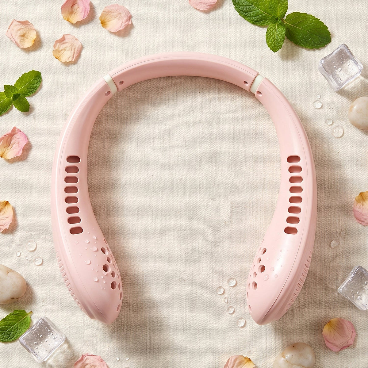 A pink portable neck fan surrounded by rose petals, mint leaves, ice cubes, and water droplets.