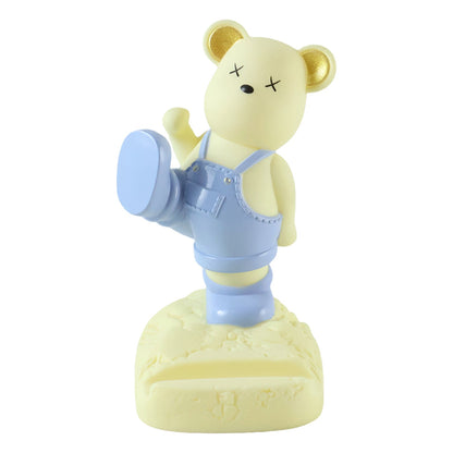 A yellow bear phone holder with blue overalls and gold ears, standing on a white background.