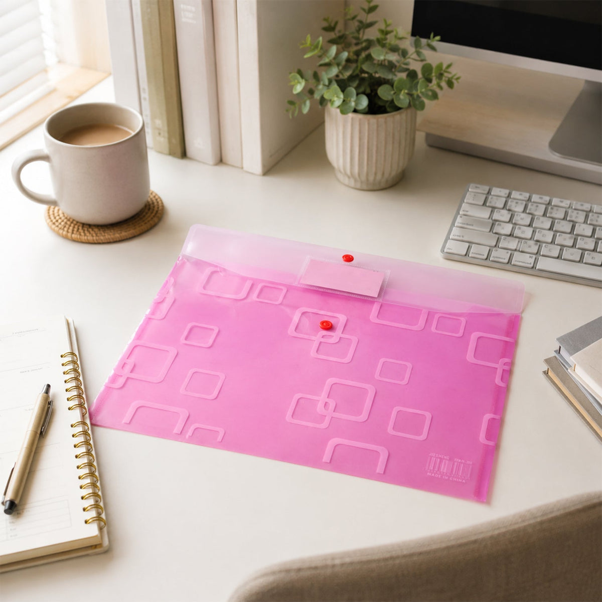 A closed pink plastic document folder on a white desk with a mug, plant, keyboard, and notebook.