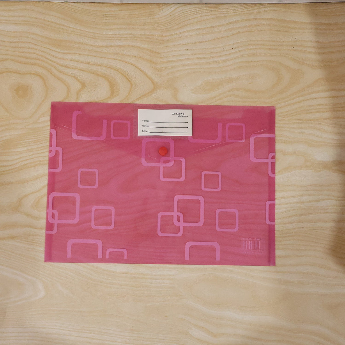 A pink plastic document folder with a button closure and a white label, centered on a light wooden surface.