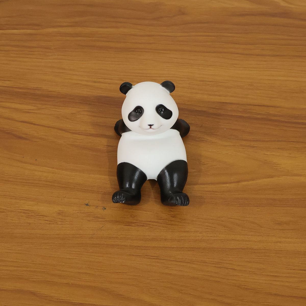 A black and white panda figurine stands upright on a wooden floor, viewed from directly above.