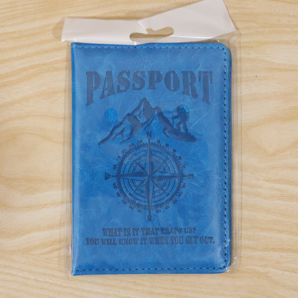 The blue passport holder with embossed design, sealed inside a clear plastic retail package.