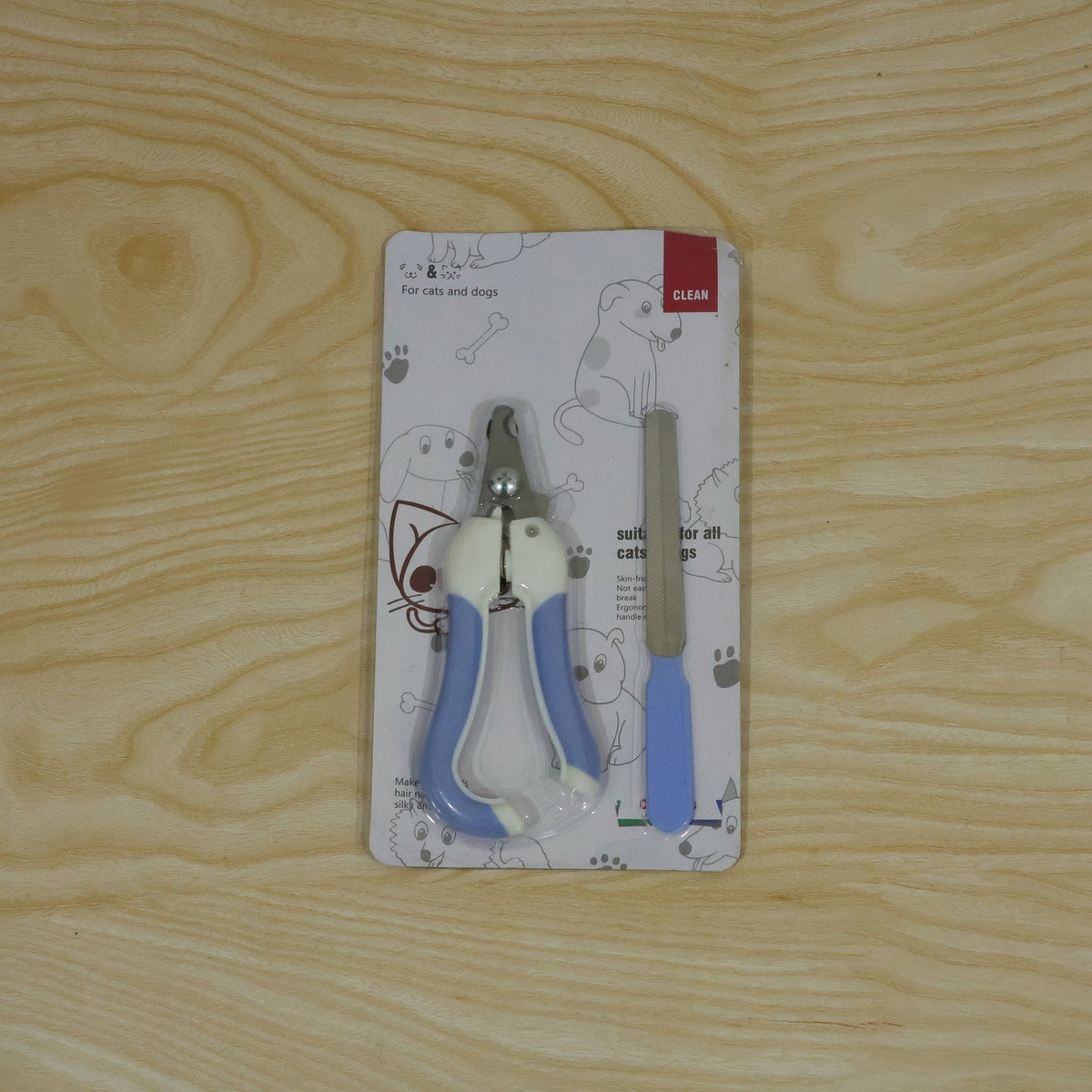 A pet nail clipper and file set in clear plastic packaging with cartoon dog and cat designs, on a wooden surface.