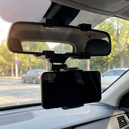 A black car phone mount attached to a rear view mirror, holding a blank smartphone screen inside a car.