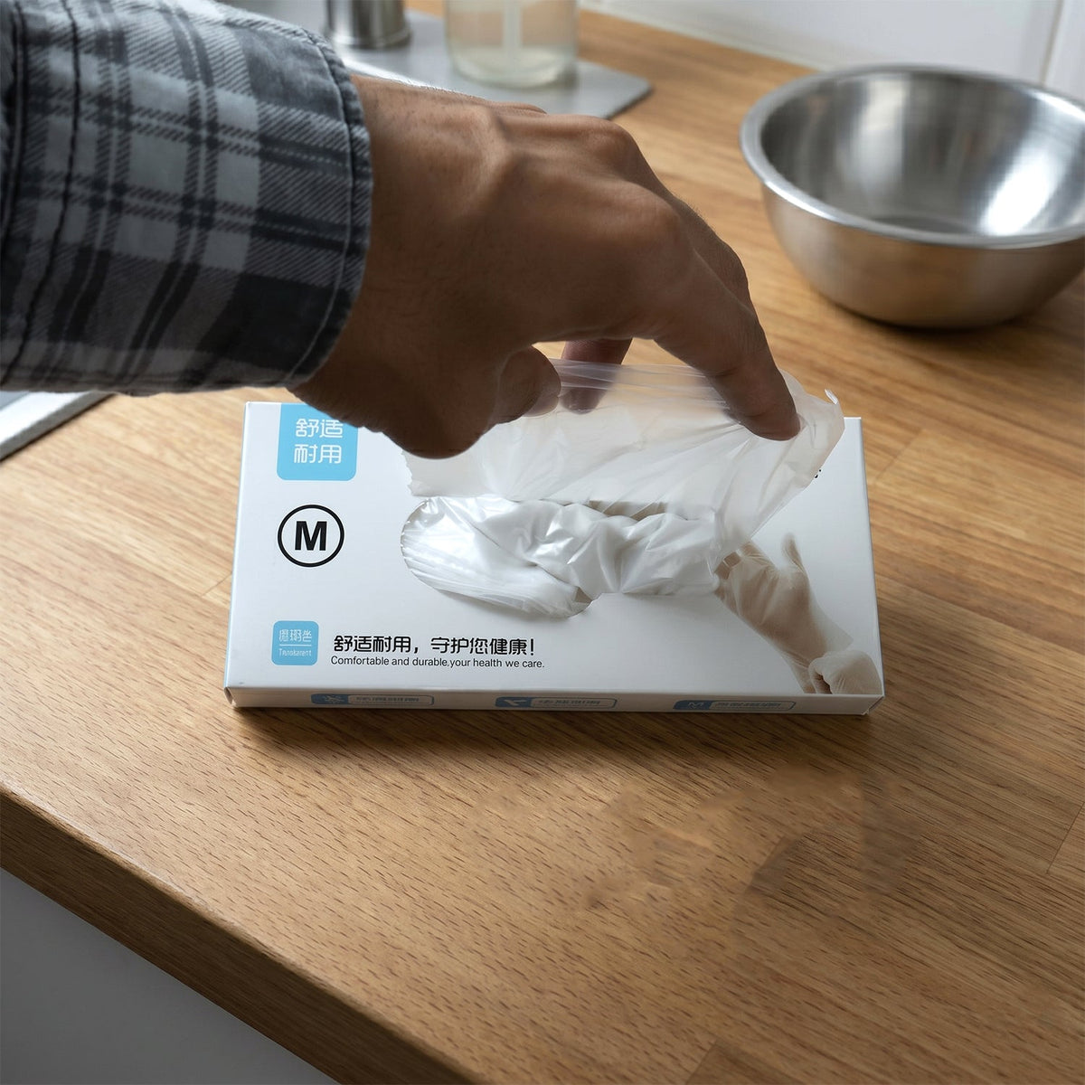 A hand pulling a clear plastic glove from a white dispenser box labeled with Chinese characters and an 'M'.