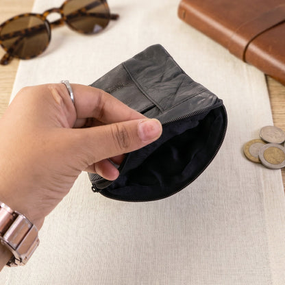 A hand opening a black leather pouch revealing its dark fabric lining, with sunglasses and coins nearby.