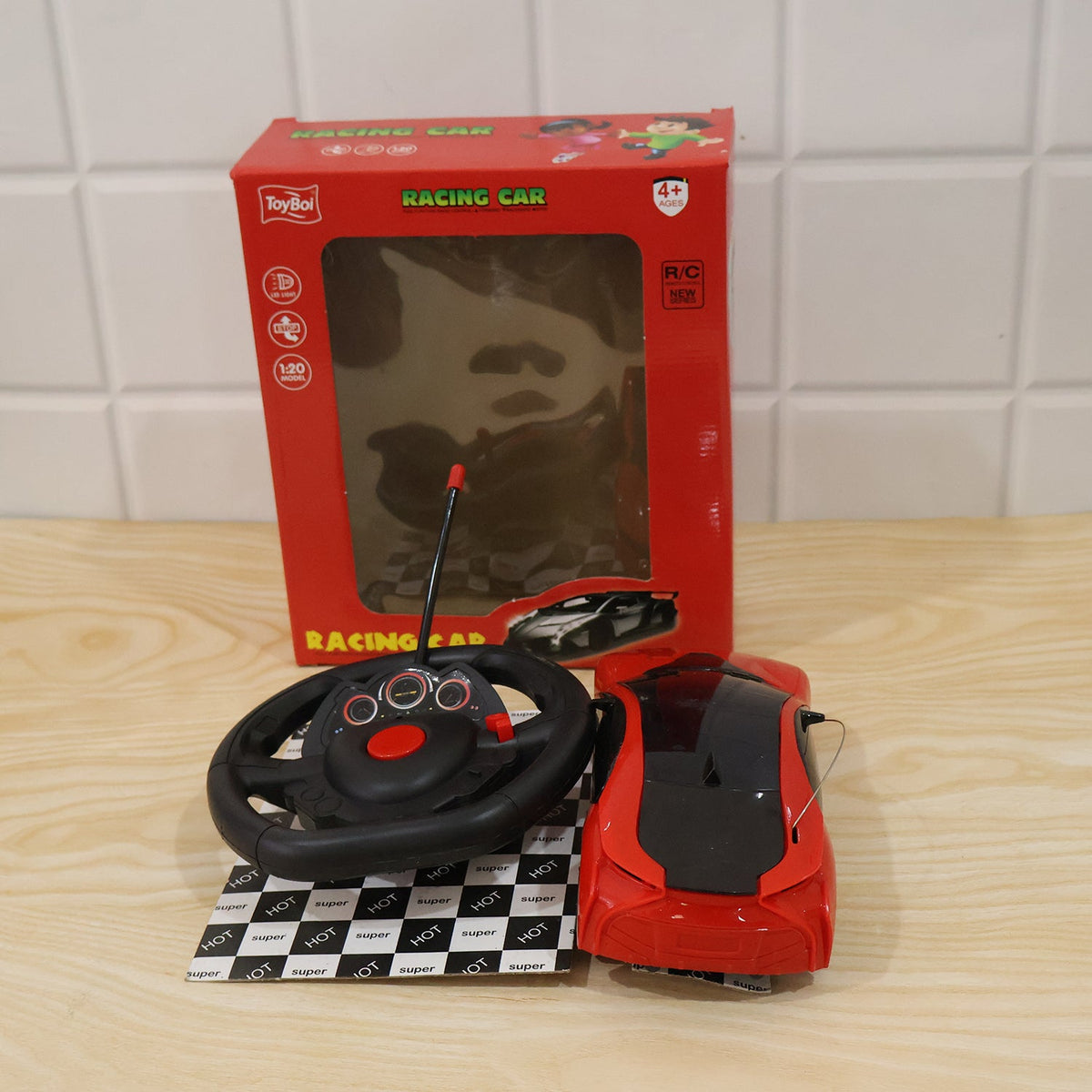 A red remote control car, its steering wheel controller, and its red packaging box are displayed on a light wooden surface.