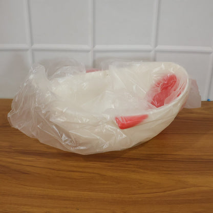 A white whale-shaped rice drainer bowl with red accents is wrapped in clear plastic packaging on a wooden surface.