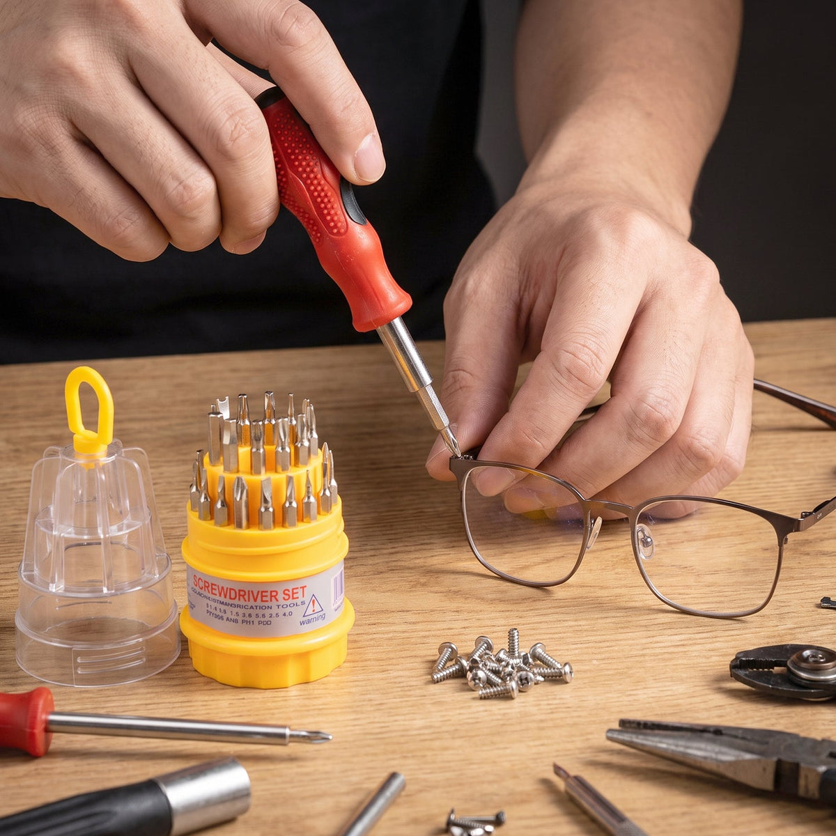 A person uses a red and black screwdriver to tighten a screw on a pair of glasses, with the screwdriver set and other tools