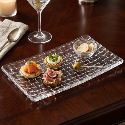 Glass serving platter with a basketweave pattern, holding assorted appetizers and a small dish of crackers.