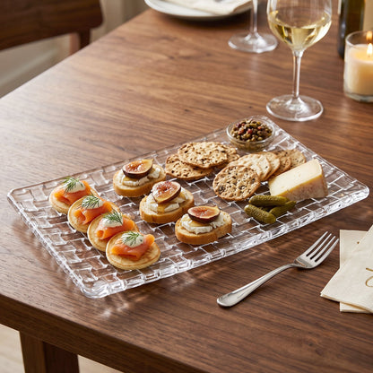 Glass serving tray with a basketweave pattern, laden with appetizers, cheese, and crackers on a wooden table.