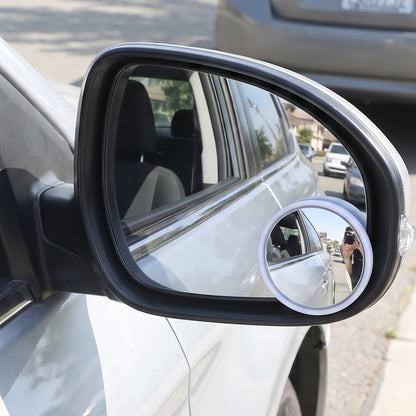 A white car's side mirror with a small round convex mirror attached, reflecting the photographer.