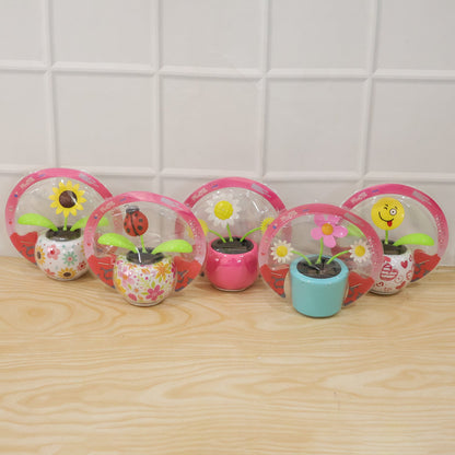 Five packaged solar dancing flowers in various designs, including a sunflower, ladybug, and winking emoji, on a wooden