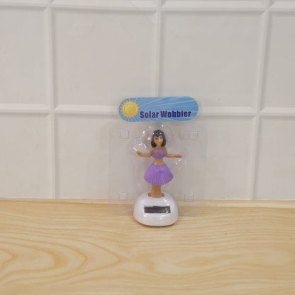 A solar-powered dancing hula girl toy in purple and brown, with a white base, in its clear plastic packaging.
