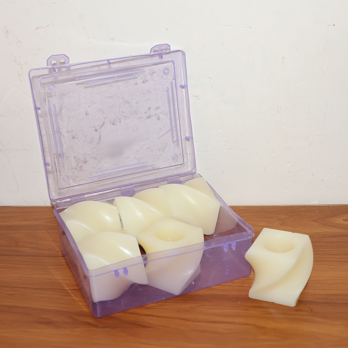 Five unlit cream-colored flameless LED candles with a twisted design are inside a clear purple plastic box, with one outside.
