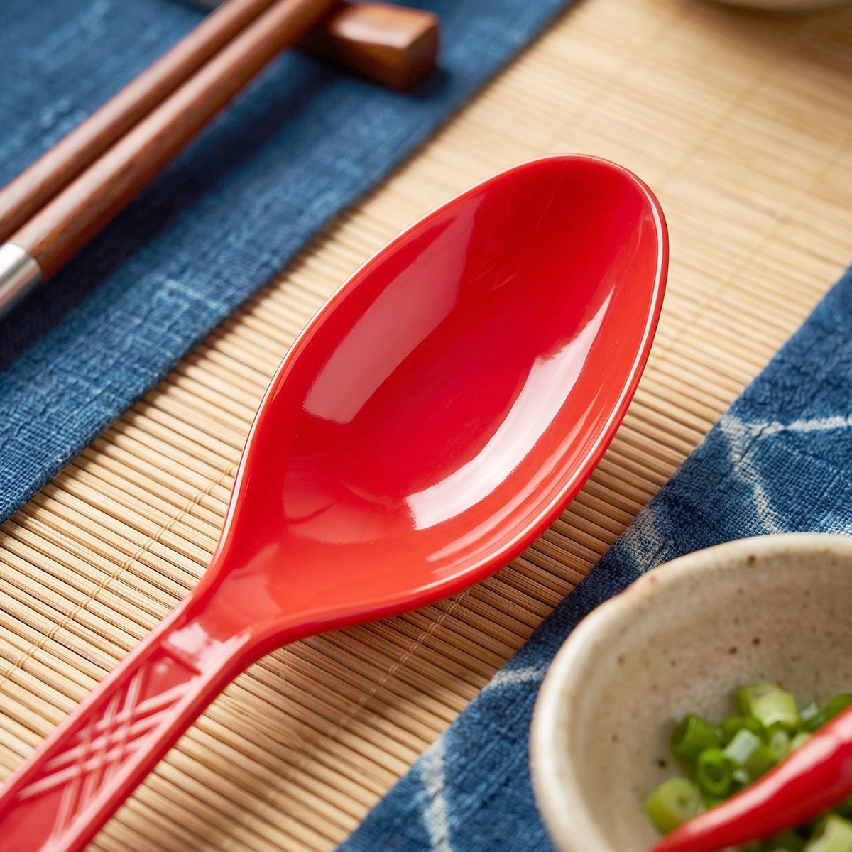 Close-up of a single red plastic spoon with a textured handle on a blue and bamboo mat.