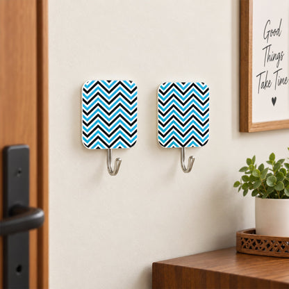 Two blue and black chevron-patterned adhesive hooks are mounted on a light wall next to a wooden door and a framed picture.
