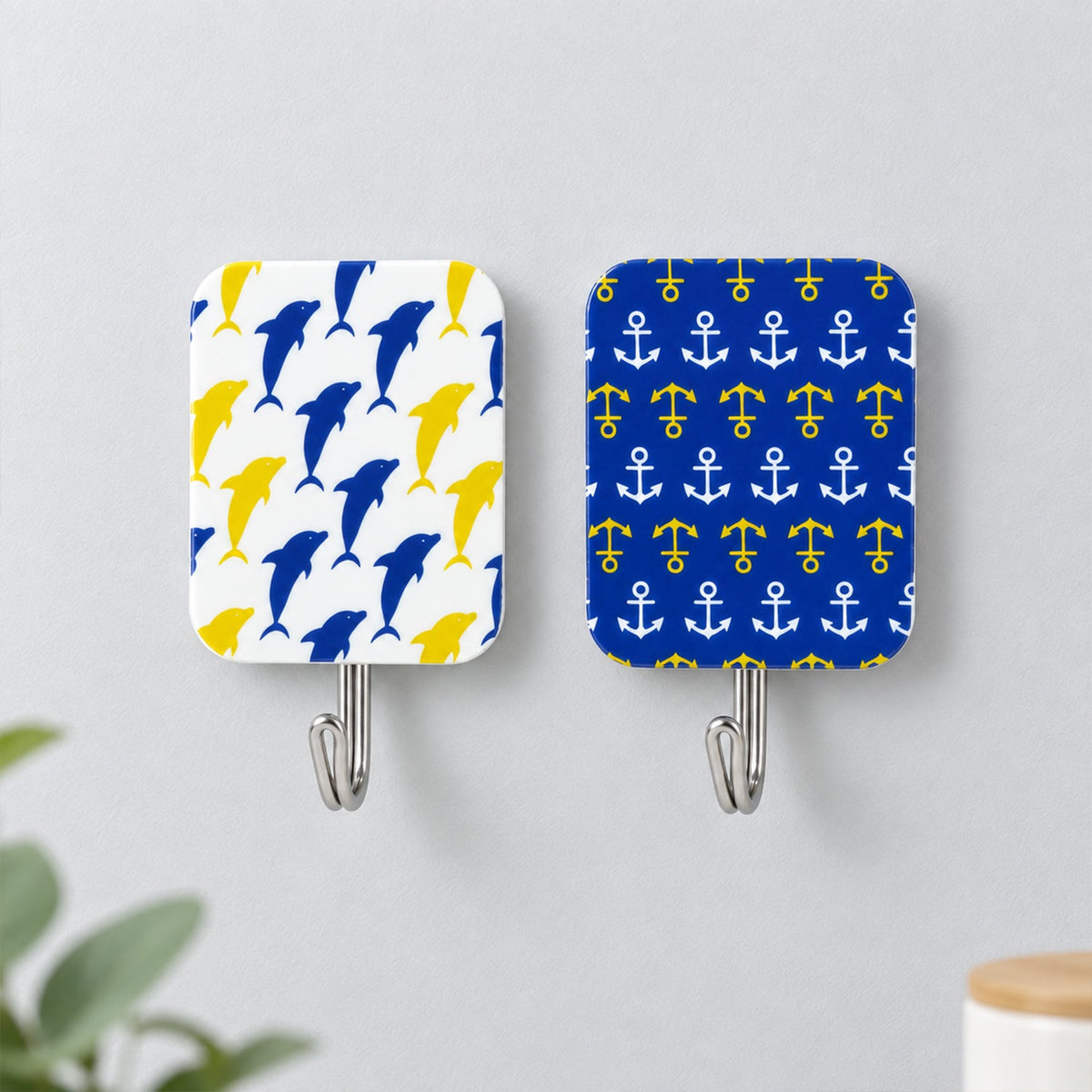 Two decorative adhesive hooks on a gray wall, one with blue dolphins, the other with yellow anchors.
