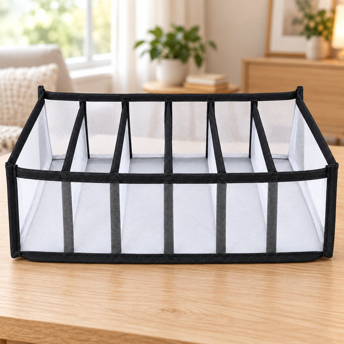 A white mesh and black fabric 6-section drawer organizer sits on a light wooden table in a bright room.