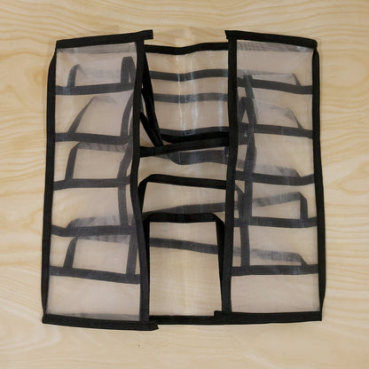 A white mesh and black fabric 6-section drawer organizer is shown folded flat on a light wooden surface.