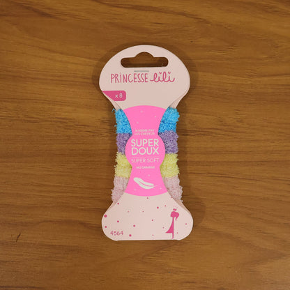A pink package of 'Princesse Lili' hair bands, labeled 'Super Doux' and 'Super Soft', sits on a wooden surface.