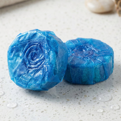Two blue toilet cleaner tablets with a spiral pattern on a wet marble counter.