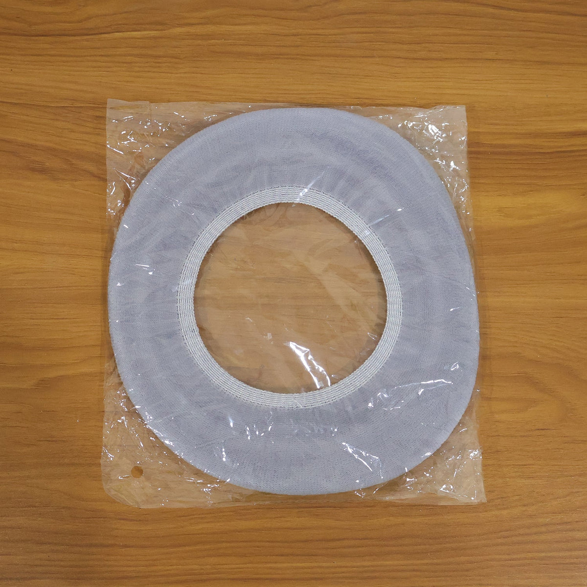 A light grey elastic toilet seat cover sealed in clear plastic packaging on a wooden surface.