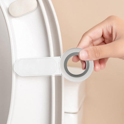 A hand holding the white and gray toilet seat lifter, attaching it to the underside of a white toilet seat.