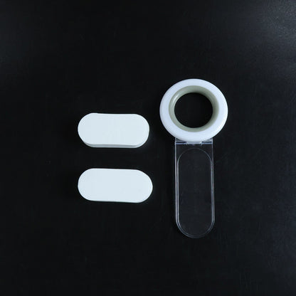 A white and gray toilet seat lifter with a clear handle and two white oval adhesive pads arranged on a dark background.
