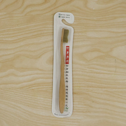 A bamboo toothbrush in clear plastic packaging with Chinese text, laid on a light wooden surface.