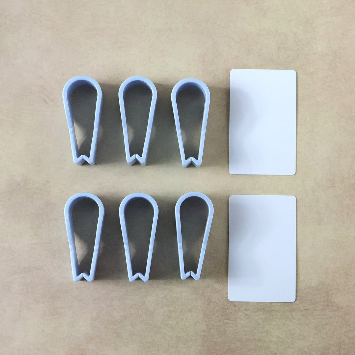Six blue plastic clips, three shaped like tweezers and three like bowties, with two white rectangular cards on a brown