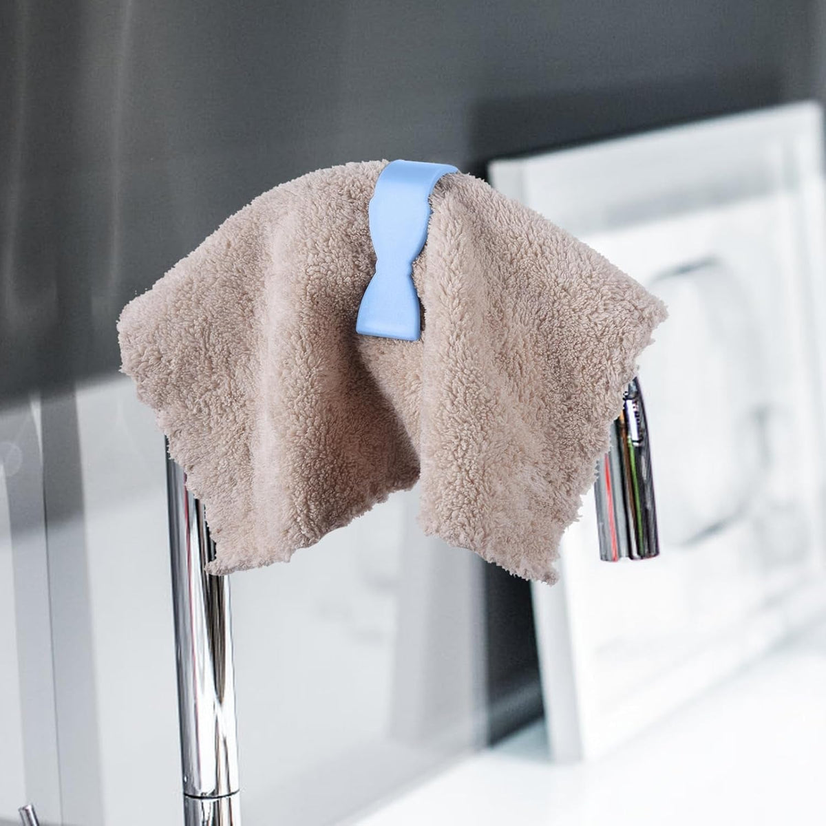 A blue towel clip holding a brown fluffy towel over a chrome faucet with water running.
