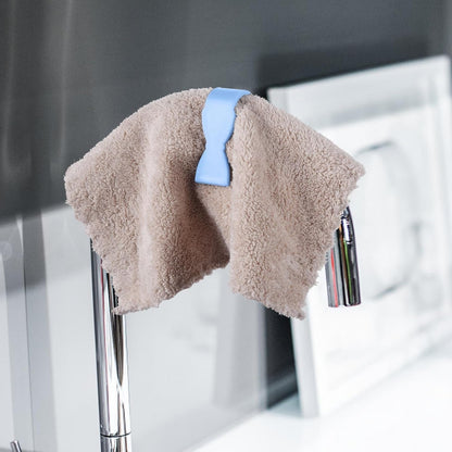 A blue towel clip holding a brown fluffy towel over a chrome faucet with water running.