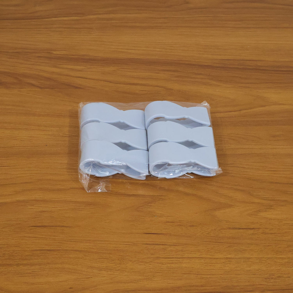 Four blue plastic towel clips, shaped like bowties, packaged in clear plastic on a wooden surface.