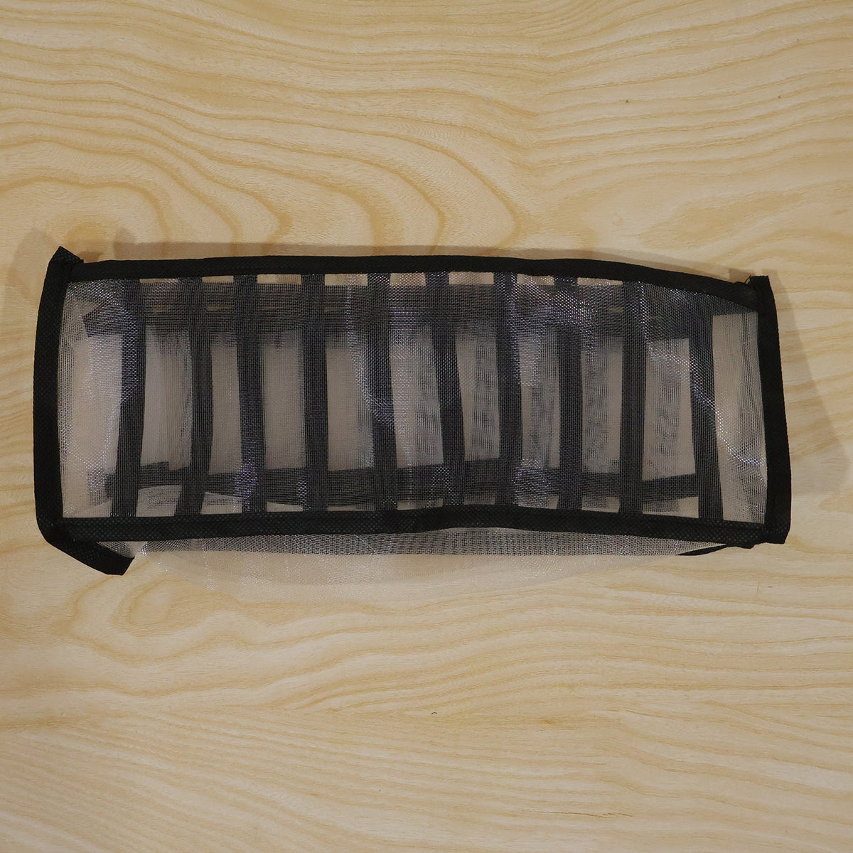 A white and black mesh fabric organizer is shown unfolded on a light wooden surface.