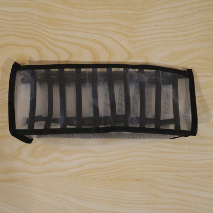 A white and black mesh fabric organizer is shown unfolded on a light wooden surface.