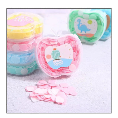 A pink apple-shaped container of paper soap sits in front of stacked containers of yellow, blue, and green soap.