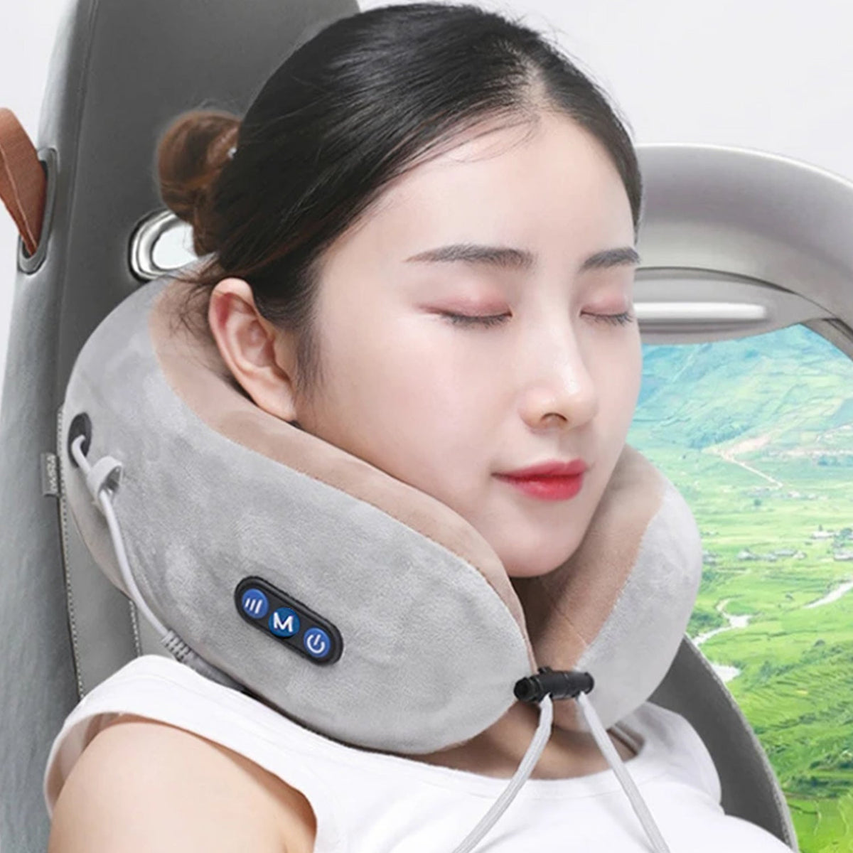 A woman with her eyes closed wears a gray and beige U-shaped massage pillow, featuring blue control buttons, in a car seat.