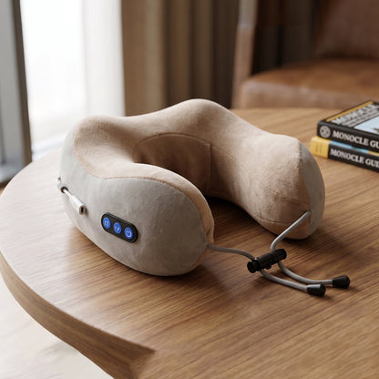 A beige and gray U-shaped massage pillow with blue control buttons and adjustable cord is displayed on a polished wooden