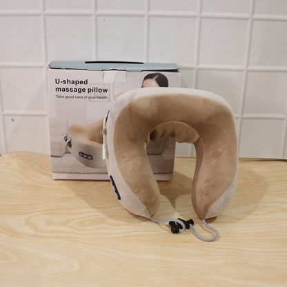 A beige and gray U-shaped massage pillow with blue controls sits on a wooden surface in front of its white product box.