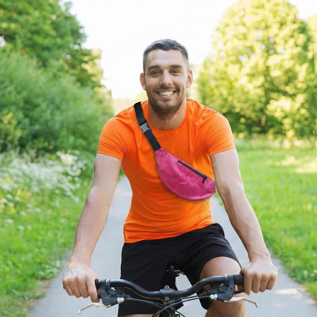 A man on a bicycle wears a pink fanny pack across his chest, smiling at the camera.