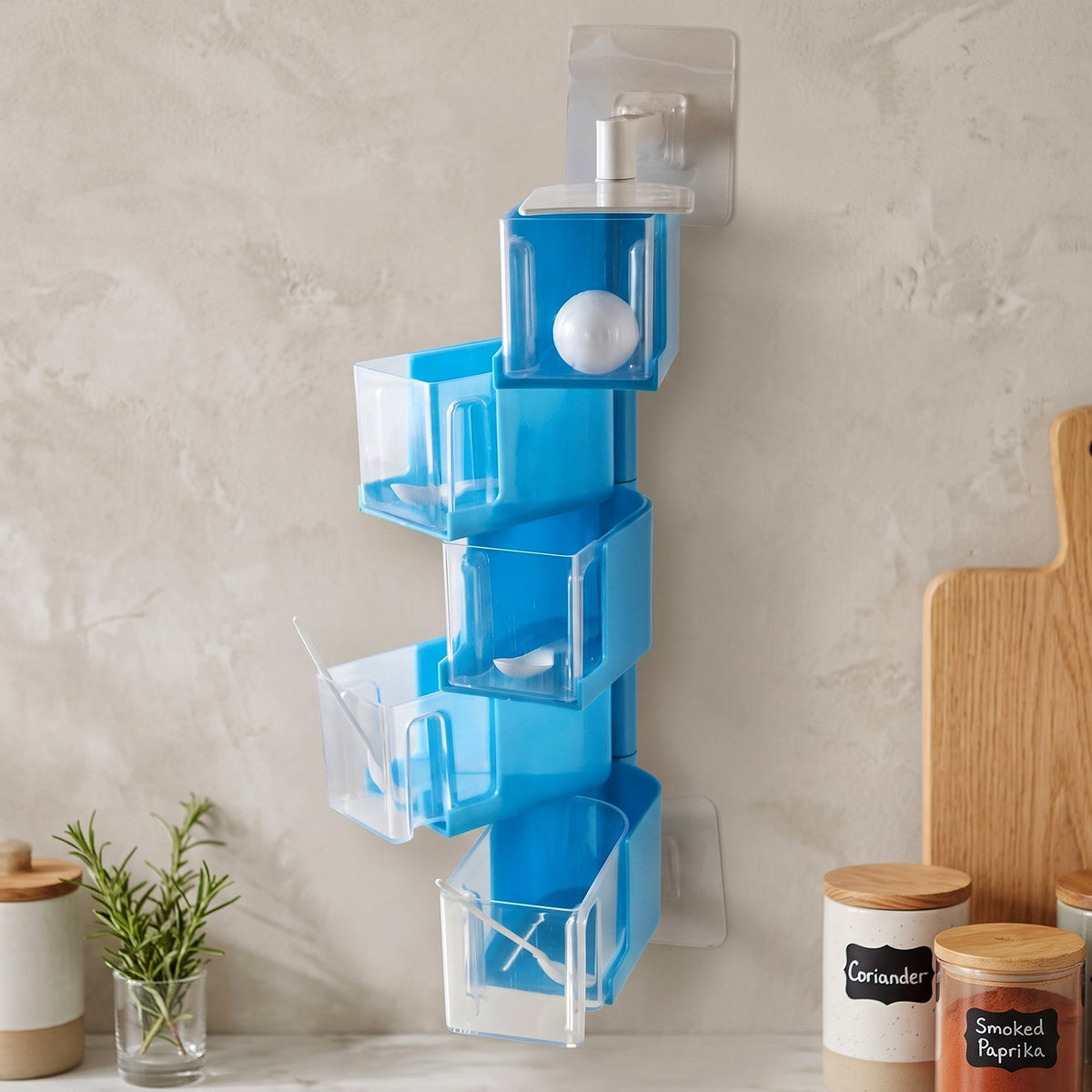 A blue 5-layer rotating spice rack with empty clear containers and small white spoons on a light gray wall.
