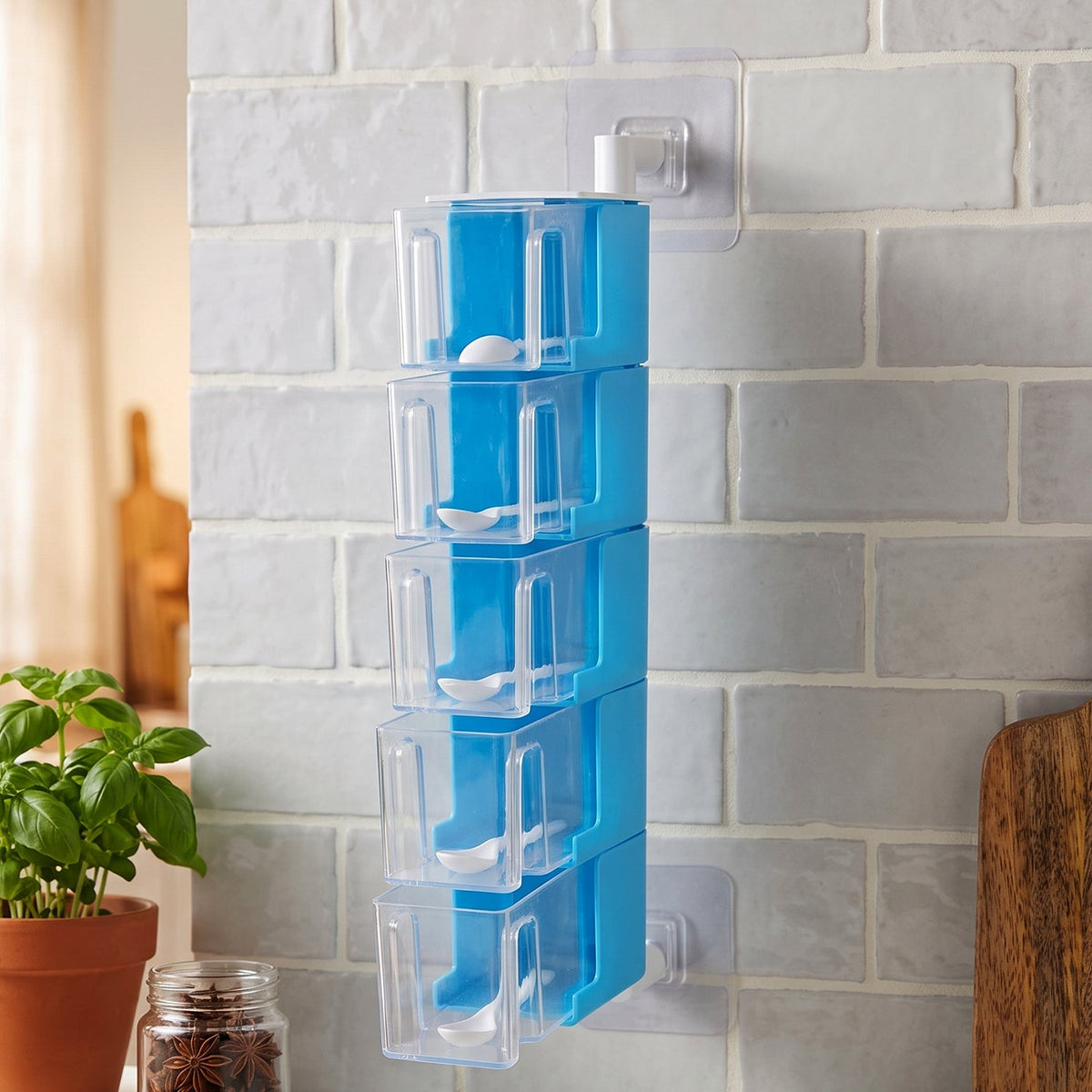 A blue 5-layer rotating spice rack with clear containers and white spoons, mounted on a light gray tiled wall.