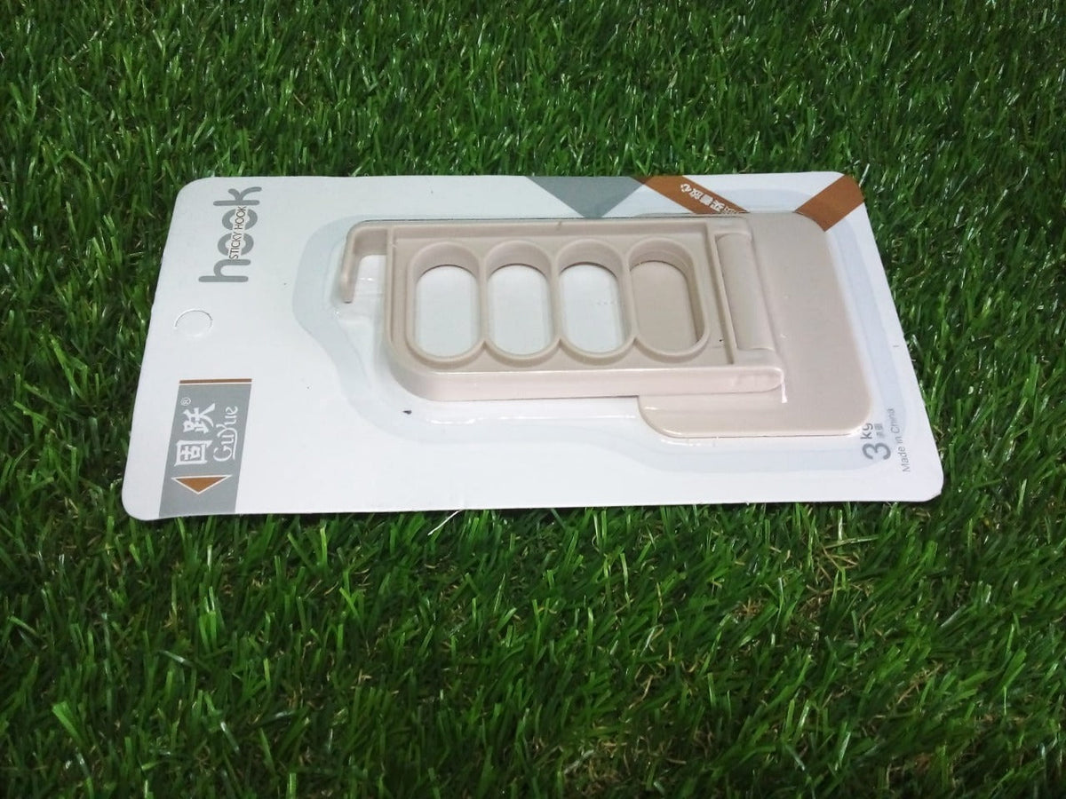A beige foldable wall hook is packaged in clear plastic on a white card, resting on green artificial grass.
